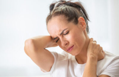 Woman with pain in the nech holding it with both arms with painful expression on her face.